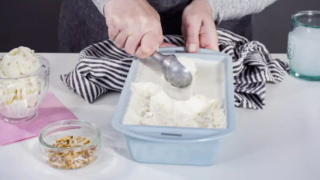 Scooping homemade coconut ice cream into a glass ice cream bowl.